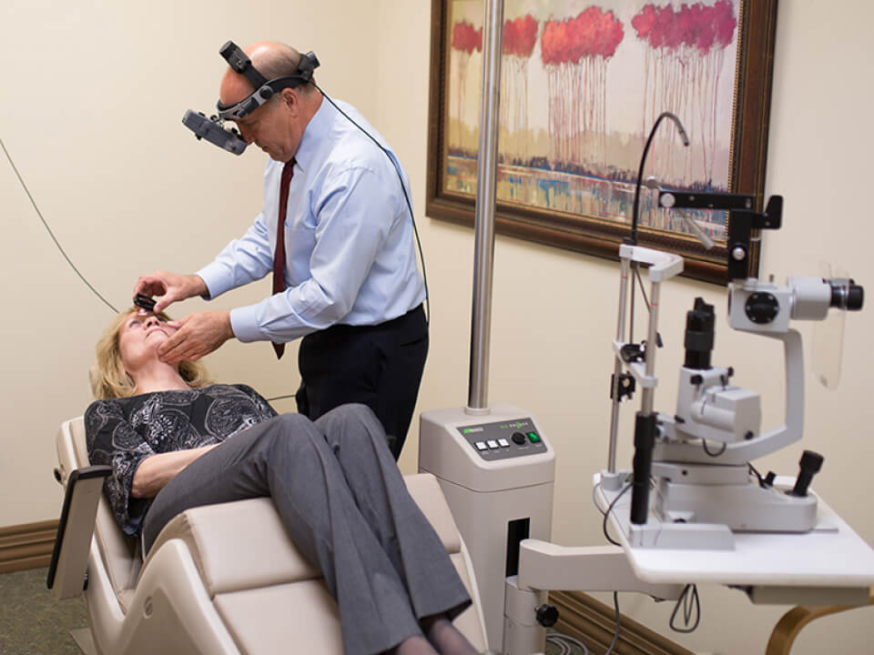 An eye doctor performing an eye examination on a patient using a slit lamp microscope in a clinic setting.