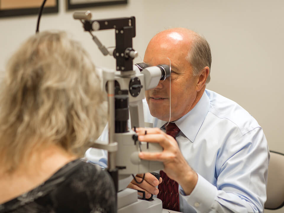 An eye doctor performing an eye examination on a patient using a slit lamp microscope in a clinic setting.