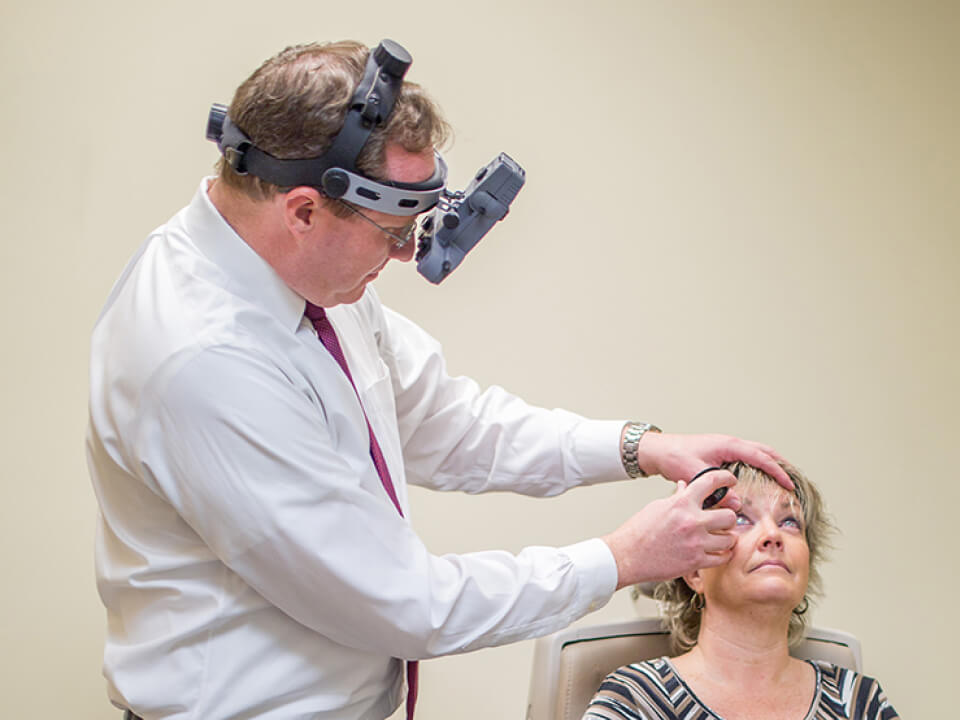 An eye doctor performing an eye examination on a patient using a slit lamp microscope in a clinic setting.