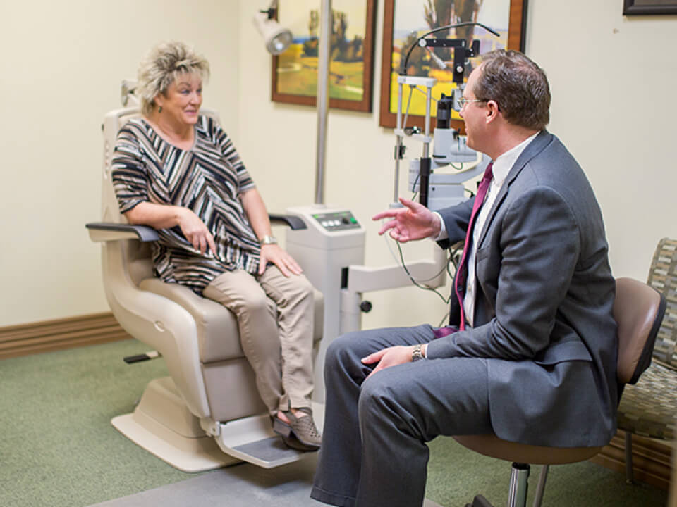 An eye doctor performing an eye examination on a patient using a slit lamp microscope in a clinic setting.