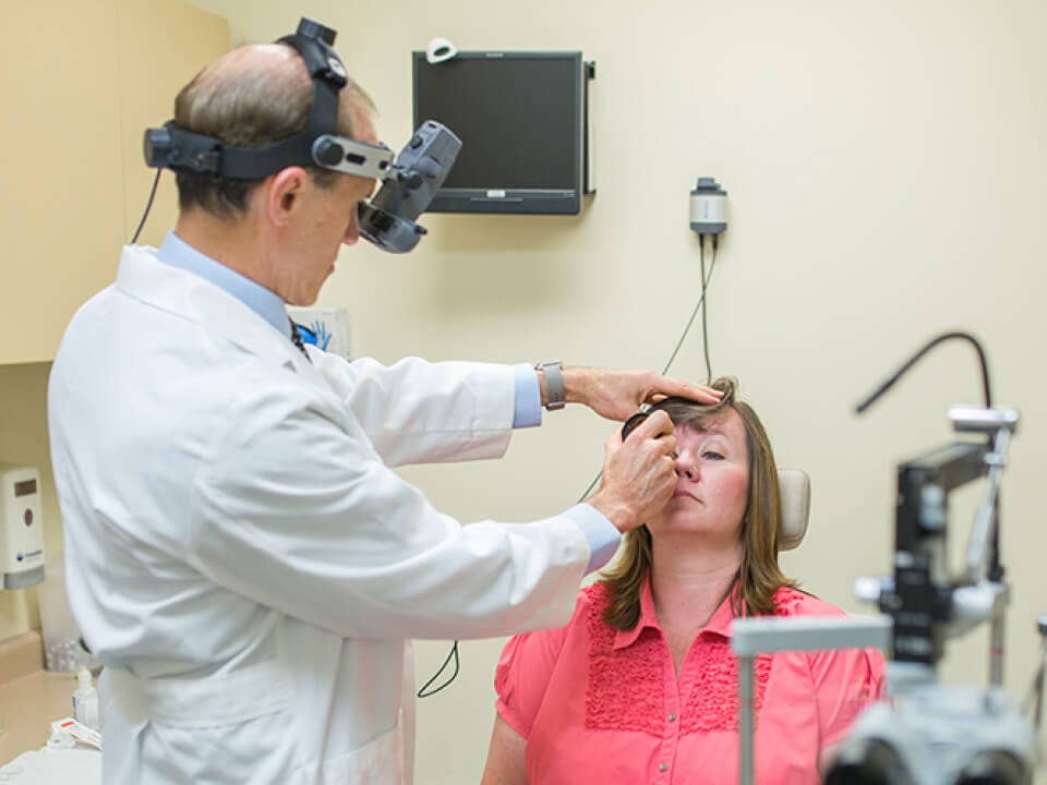 An eye doctor performing an eye examination on a patient using a slit lamp microscope in a clinic setting.