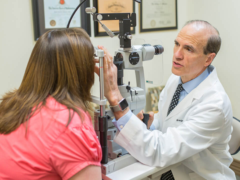 An eye doctor performing an eye examination on a patient using a slit lamp microscope in a clinic setting.
