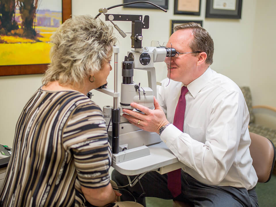 An eye doctor performing an eye examination on a patient using a slit lamp microscope in a clinic setting.